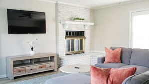Una sala de estar con chimenea, un televisor de pantalla plana, un sofá gris y un mueble de entretenimiento de madera.