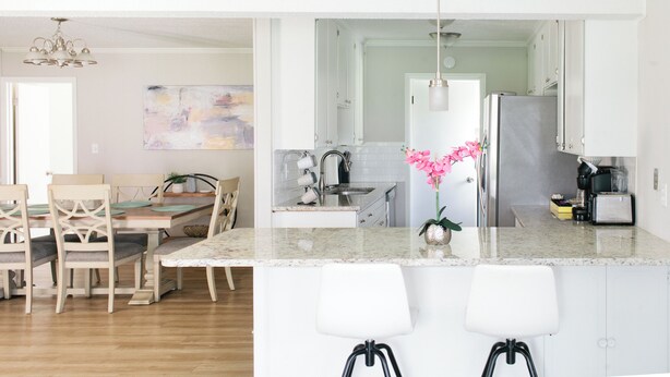 Una cocina moderna con una isla central, muebles blancos y una zona de comedor con sillas y mesa de madera.