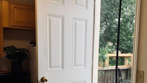 A white door with a brass doorknob, leading to a wooden deck with a view of trees. - Pet-Friendly, Lovely Studio w/ Balcony (Halifax)