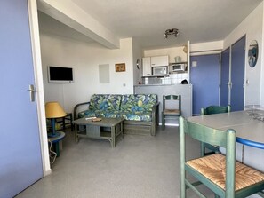 A compact living space with a sofa, a dining table, a chair, a television, and a kitchenette.