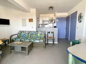 A compact living space with a sofa, a small table, a chair, a kitchenette, and a door.