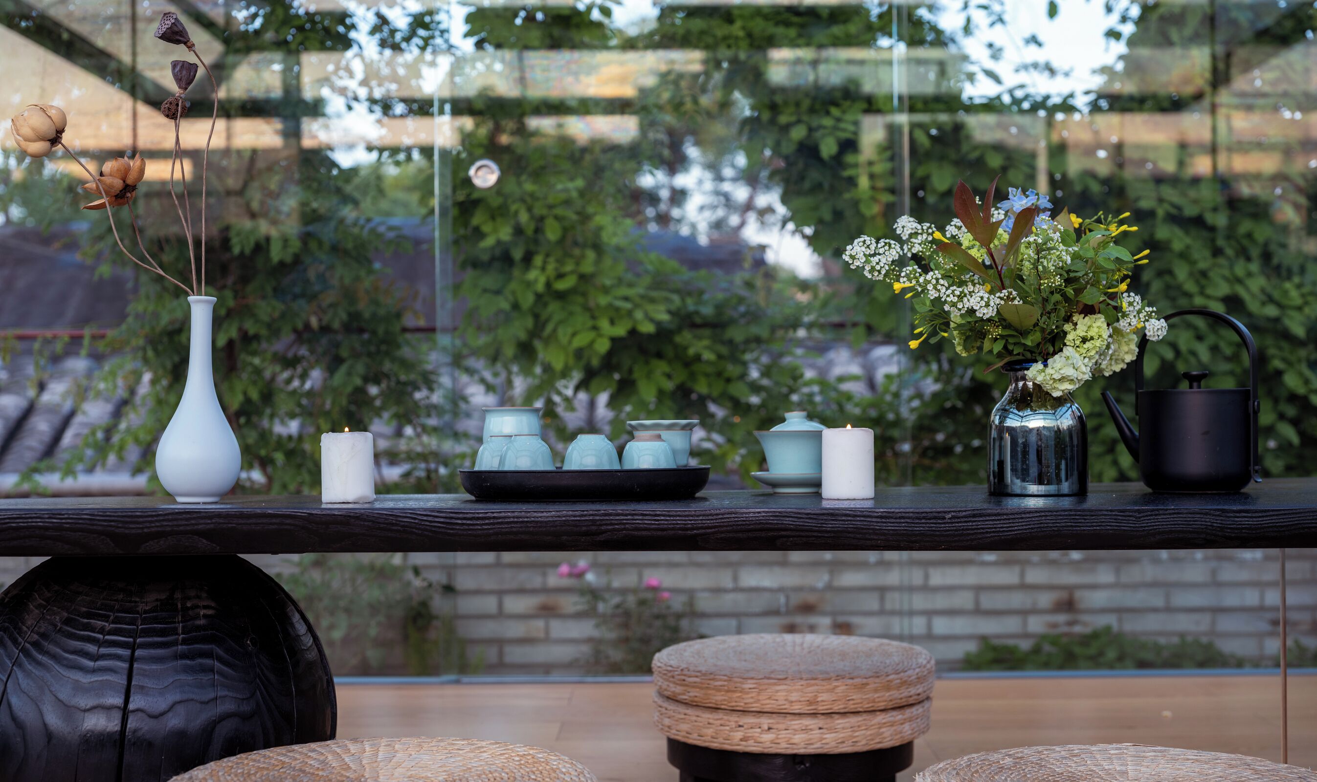 A table with a vase, candles, a metal watering can, and a tray with teapots.