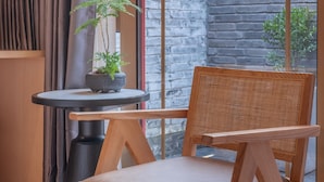 A modern room with a wooden chair, a small table with a potted plant, and a view of a brick wall and greenery outside. - XinXiangYaYuan Courtyard (Beijing)