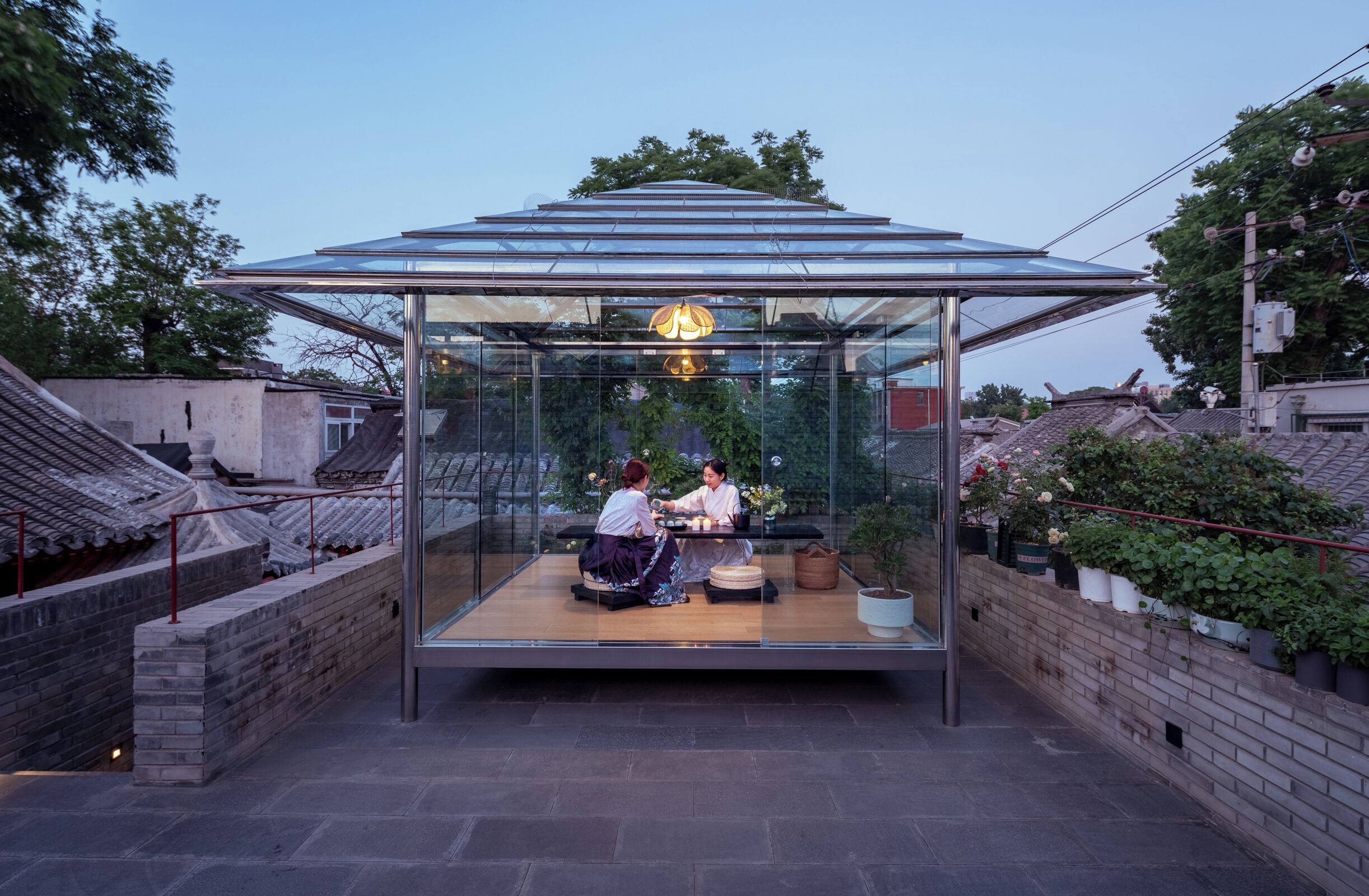 Una casa de té japonesa tradicional con techo de cristal, que presenta una mesa de madera baja y dos personas sentadas en su interior.