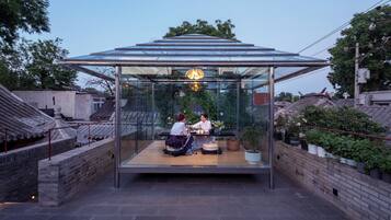 Una casa de té japonesa tradicional con techo de cristal, que presenta una mesa de madera baja y dos personas sentadas en su interior.
