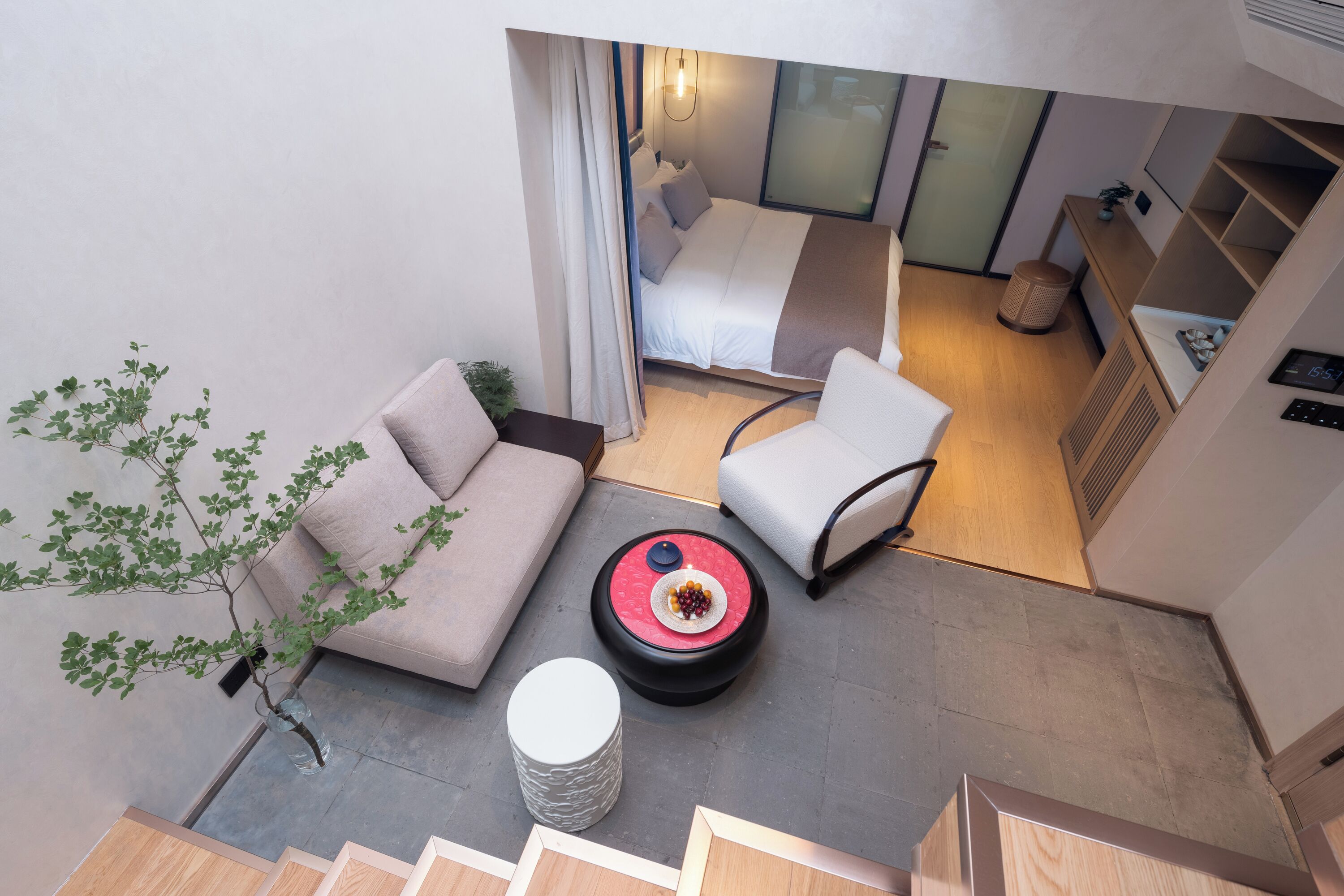 Una habitación de hotel moderna con una cama, un sofá, una silla, una mesita con un frutero y una planta en maceta.
