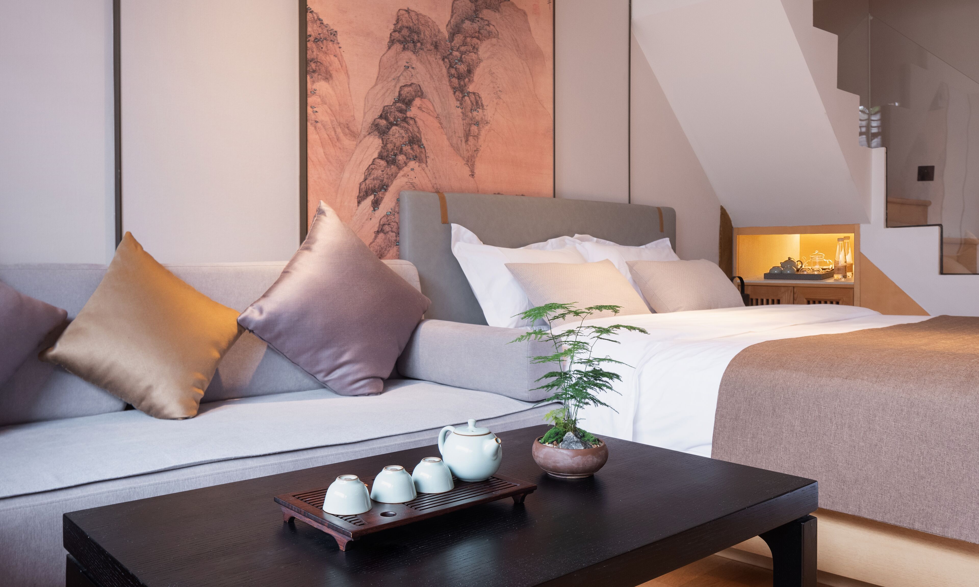 Une chambre d’hôtel moderne, équipée d’un canapé, d’un lit, d’une table de chevet et d’une table basse sur laquelle sont posées des théières.