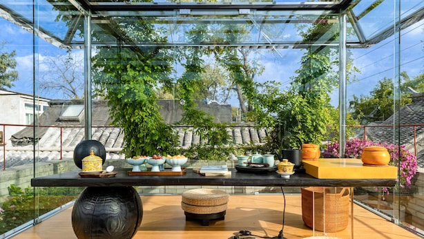 A modern interior with a glass enclosure, a wooden table with various items, and a view of greenery outside. - XinXiangYaYuan Courtyard (Beijing)
