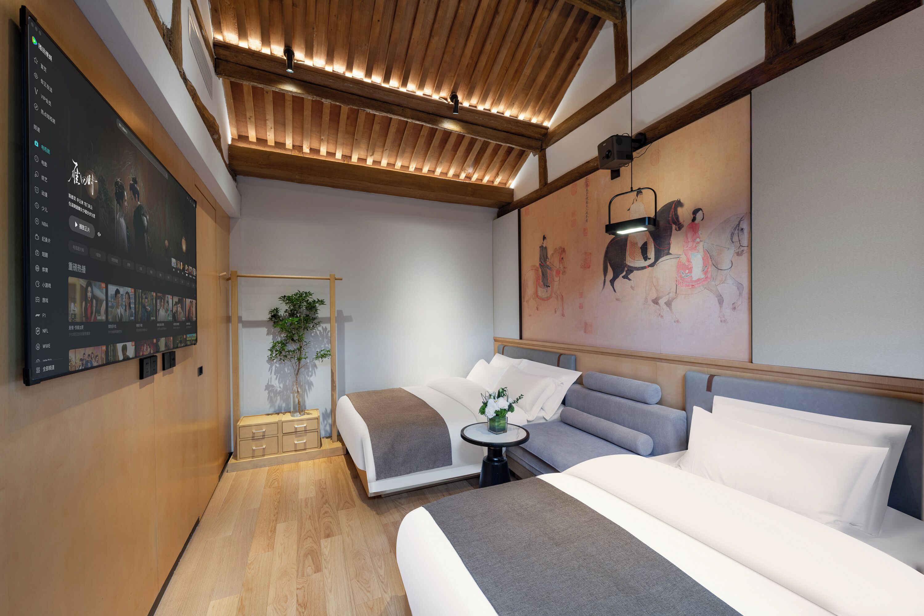 A modern hotel room with a large bed, a sofa, a small table, and a wall-mounted TV displaying a movie.