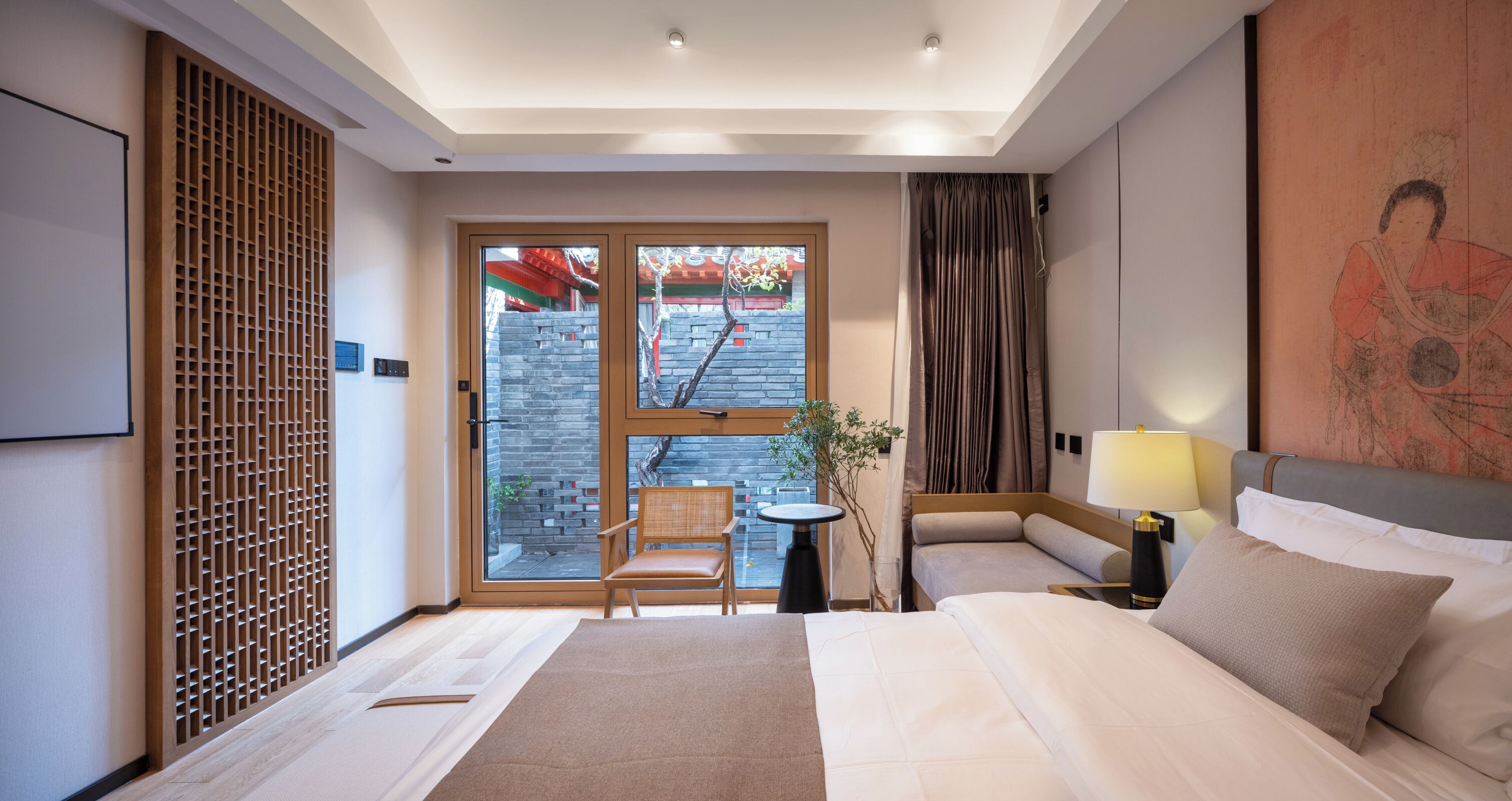 Ein Hotelzimmer mit einem Bett, zwei Nachttischen, einem Sessel, einem Fenster mit Blick auf eine Ziegelwand und Bäume sowie einer Wandverkleidung.