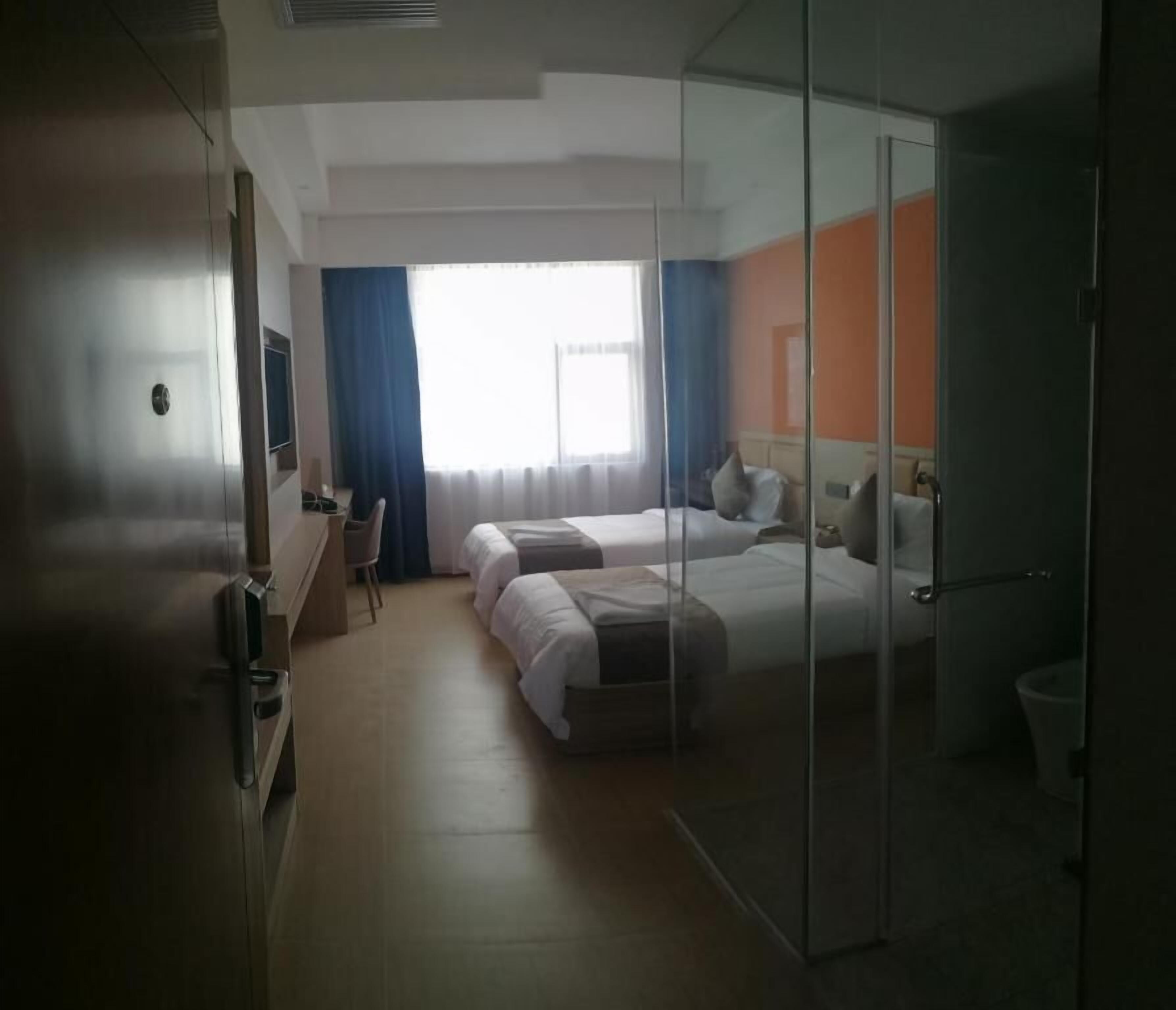 A hotel room with two beds, a desk, a chair, a TV, and a large window with curtains.
