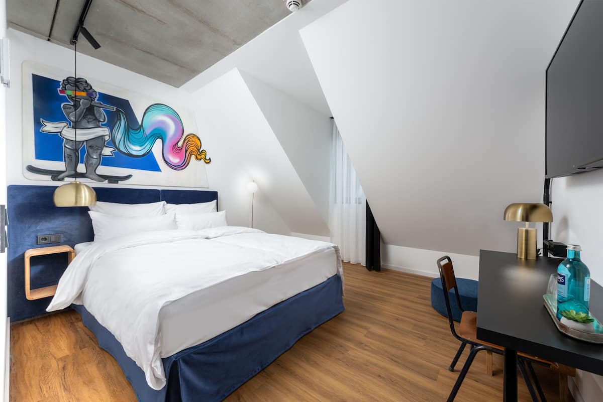 Une chambre moderne avec un lit, un bureau et une chaise. Il y a un tableau au mur et un ventilateur de plafond.