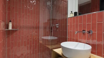 Un baño moderno con ducha envuelta en vidrio, un lavamanos blanco y paredes con azulejos rojos.