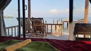 A room with a bed, a wooden chair, and a view of the sea and pier. - Freedom Beach Resort (Phu Quoc)