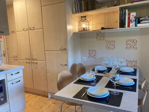 A modern kitchen with a dining area set for four, featuring a granite countertop, wooden cabinets, and a tiled backsplash. - Cozy 2-bedroom Apt, 4/5 people, In the heart of Avoriaz (Avoriaz)