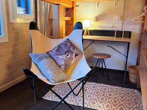 A modern room with a curved white chair, a small round table, a pegboard wall, and a wooden desk.