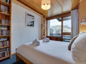 A bedroom with a bed, a bookshelf, a framed picture, and a window with a view.
