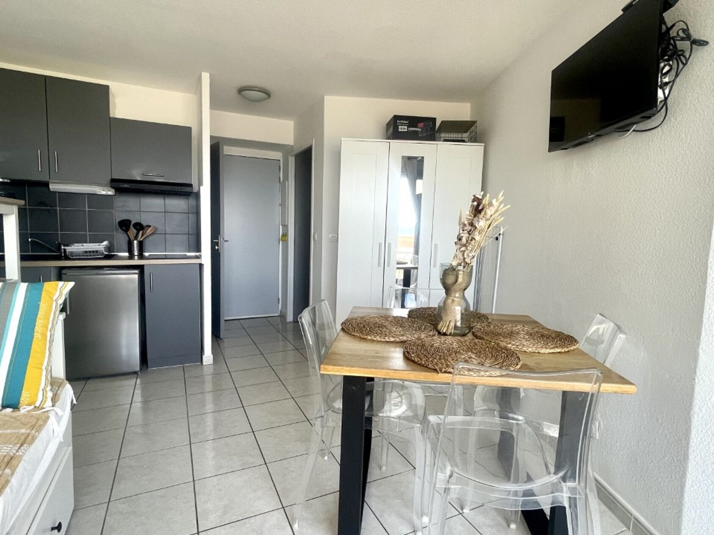 Una cocina moderna con armarios grises, un horno empotrado y un comedor con mesa de madera y sillas transparentes.