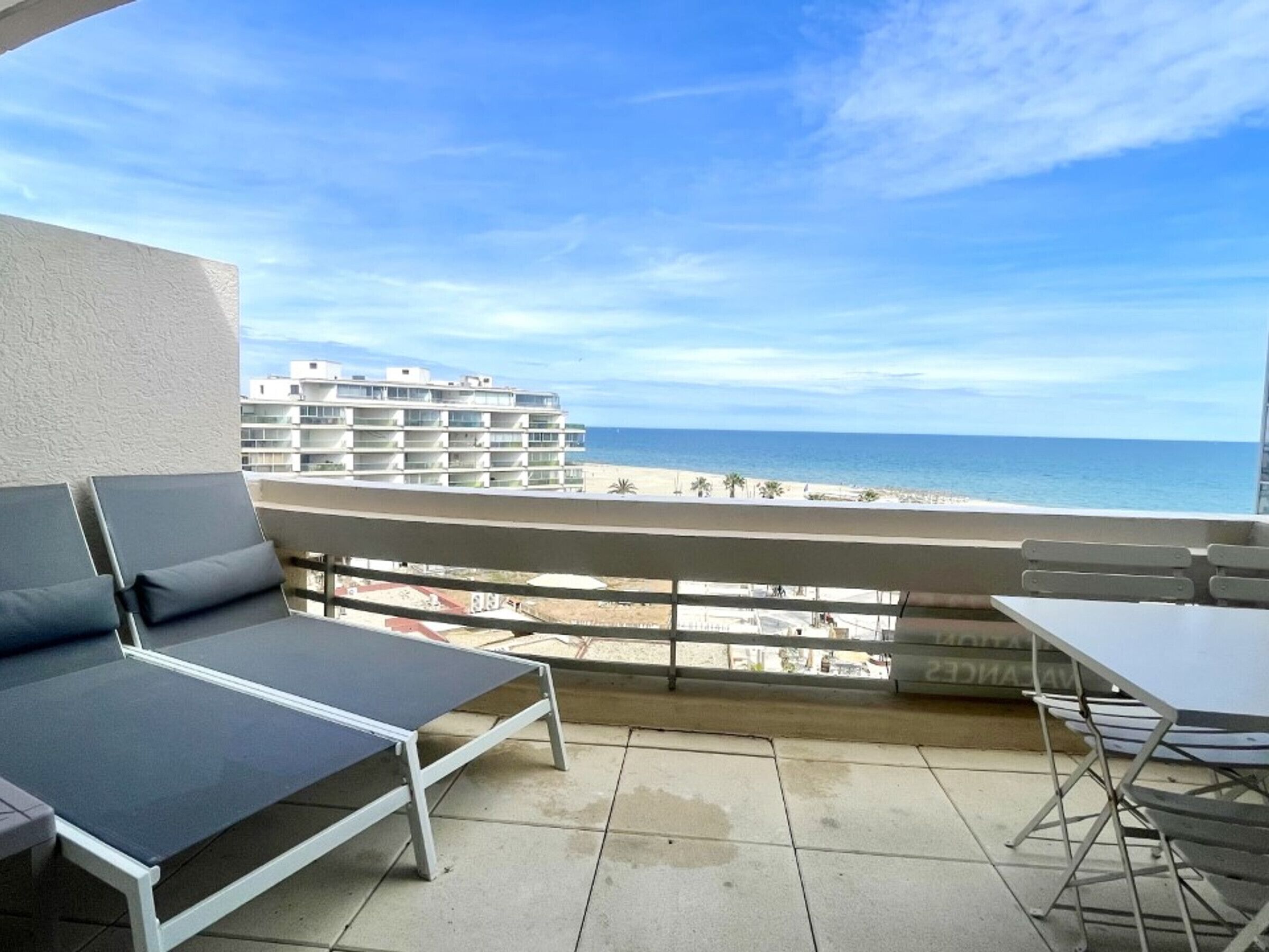 Un balcone con vista sulla spiaggia e sull'oceano, una sedia a sdraio e un tavolo.