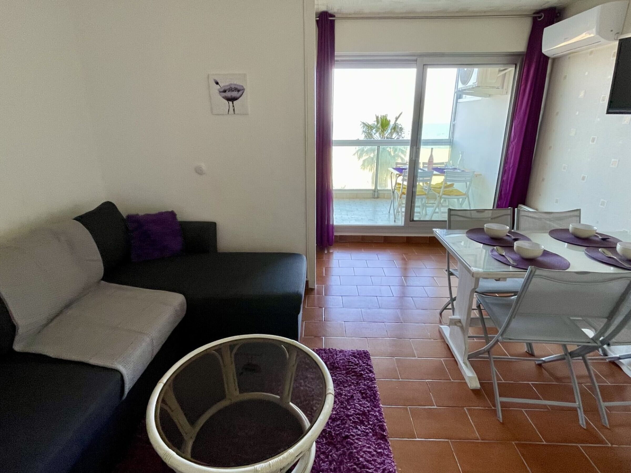 Ein Wohnzimmer mit einer Couch, einem Esstisch mit Stühlen und Blick ins Freie durch eine Glastür.