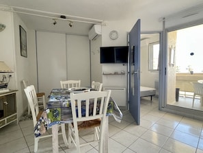A compact dining area with a table and chairs, a television mounted on the wall, and a sliding door leading to an outdoor area.