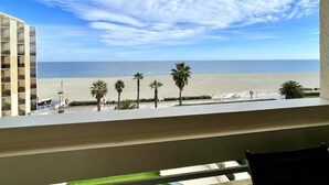 A view from a window overlooking a beach with palm trees and a clear sky.