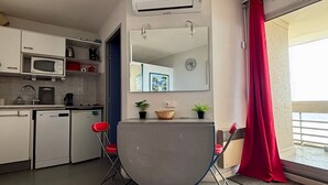 A compact kitchen with a microwave, coffee maker, and a small refrigerator. There is a dining area with a table and chairs, and a large mirror above it.