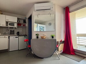 A compact kitchen with a microwave, coffee maker, and a small refrigerator. There is a dining area with a table and chairs, and a large mirror above it.