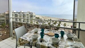 A balcony with a table set for dining, overlooking a beach and cityscape. - Stunning apartment with AC and terrace in Canet-en-Roussillon (Canet-en-Roussillon)