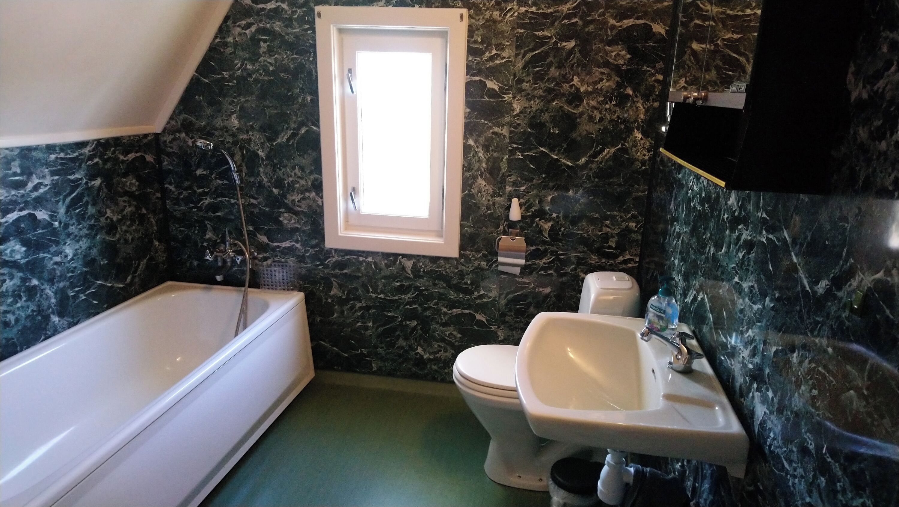 A bathroom with a bathtub, toilet, and sink, all against a dark marble wall.