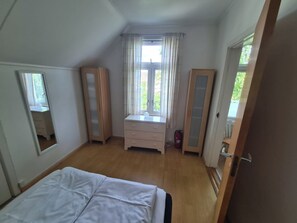 A bedroom with a bed, a dresser, a mirror, and a window with curtains. - Villa Sommerfryd Seterveien (Oslo)