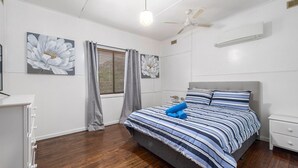 A bedroom with a bed, a nightstand, a dresser, a ceiling fan, and a window with curtains.