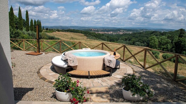 Un jacuzzi con cubierta de madera y asientos, rodeado de grava y plantas en macetas, con vistas a un paisaje pintoresco.