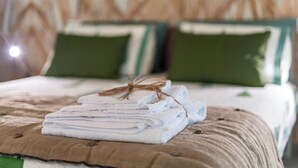 Una cama bien hecha con una toalla blanca doblada y una manta marrón, almohadas verdes y un hilo rústico atado a la toalla.