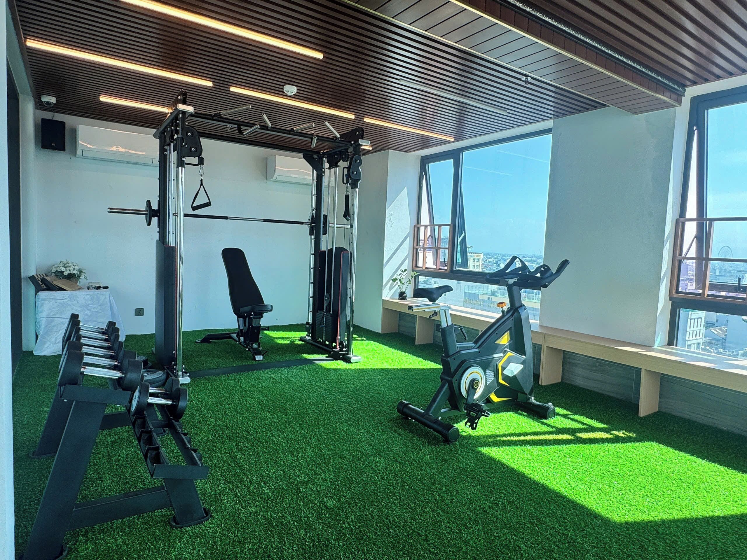 A gym with exercise equipment, a treadmill, and a view of the city through large windows.