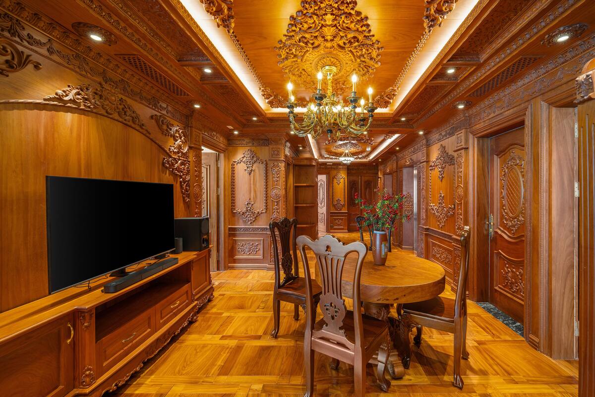 A luxurious dining area with a large chandelier, ornate wooden paneling, and a television on the left.
