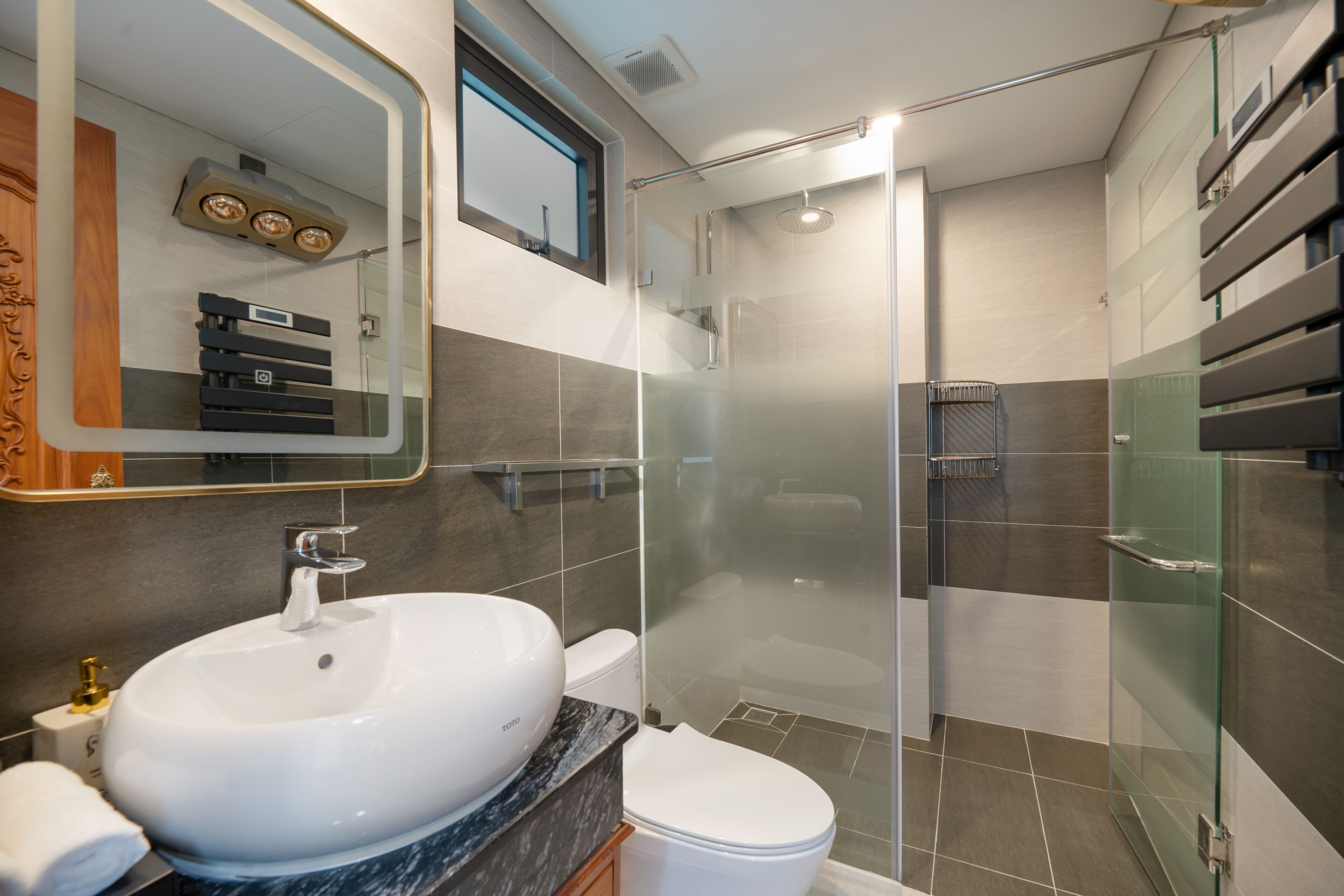 Un baño moderno con un lavamanos blanco, un inodoro y una zona de ducha con mampara de vidrio.