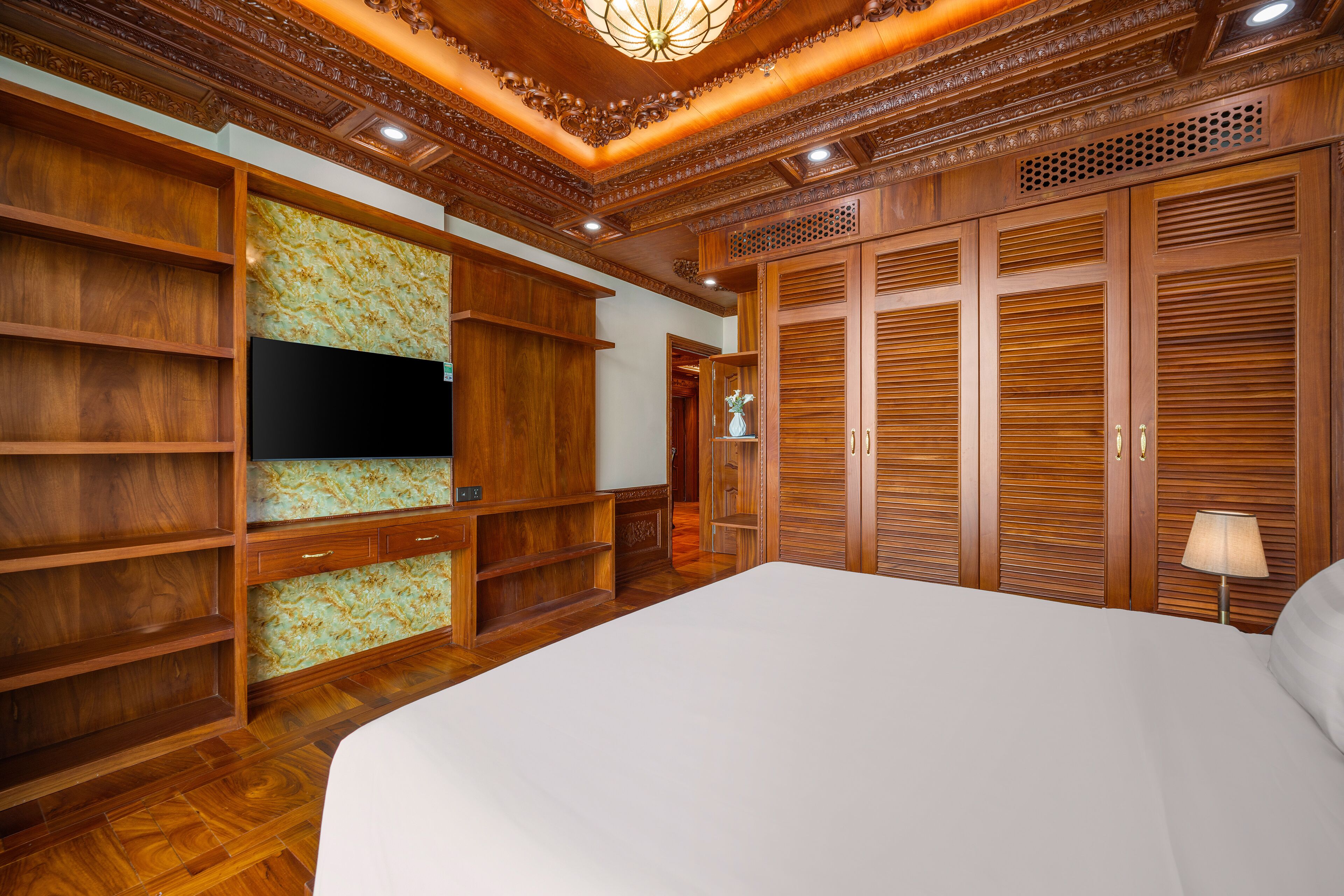 Un dormitorio con una cama grande, armario de madera, estanterías empotradas, televisor de pantalla plana y techo decorativo.