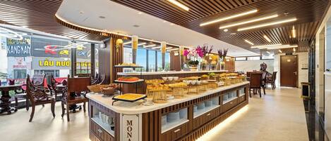 A modern buffet area with a wooden counter labeled "MONALISA," featuring various food items and a seating area with chairs.