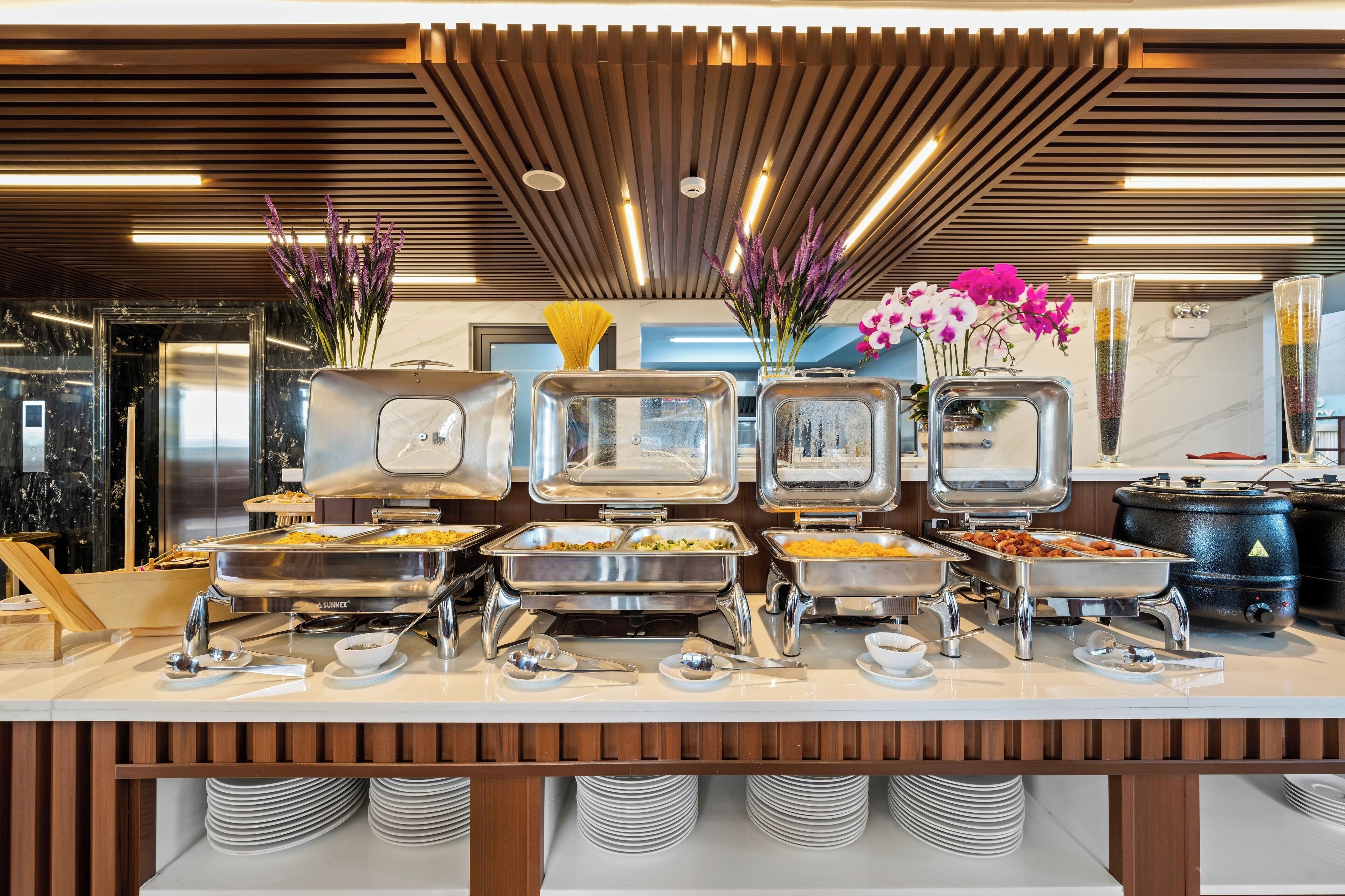 Montaje de bufé con varias estaciones de servicio, incluyendo bandejas de comida y flores decorativas.