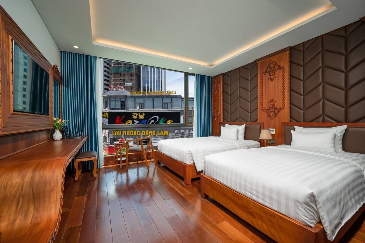 A hotel room with two beds, a desk, and a view of a cityscape.