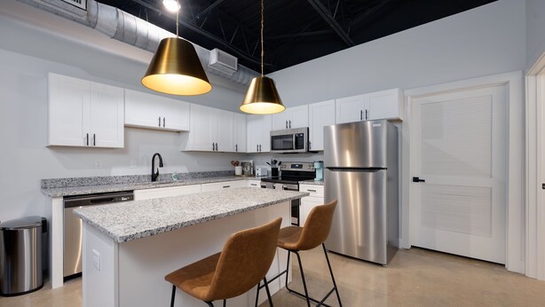A modern kitchen with white cabinets, stainless steel appliances, a granite countertop, and two bar stools.