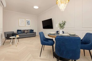 Ett modernt vardagsrum med en grå soffa, blå stolar, ett matbord med tallrikar och en vas med blommor samt en platt-TV som är monterad på väggen.