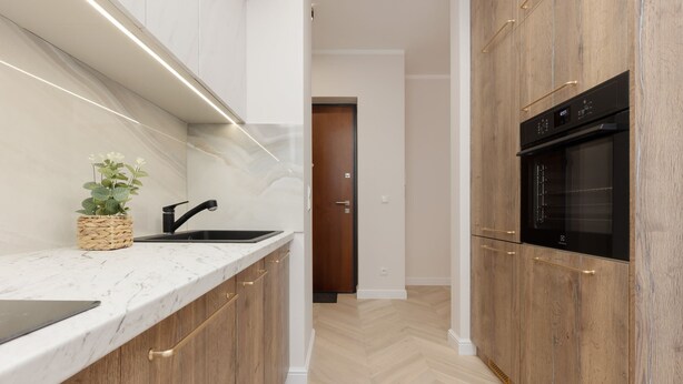 A modern kitchen with marble countertops, wooden cabinets, a built-in oven, and a herringbone-patterned floor.