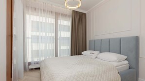 A bedroom with a bed, a window with sheer curtains, and a light fixture.