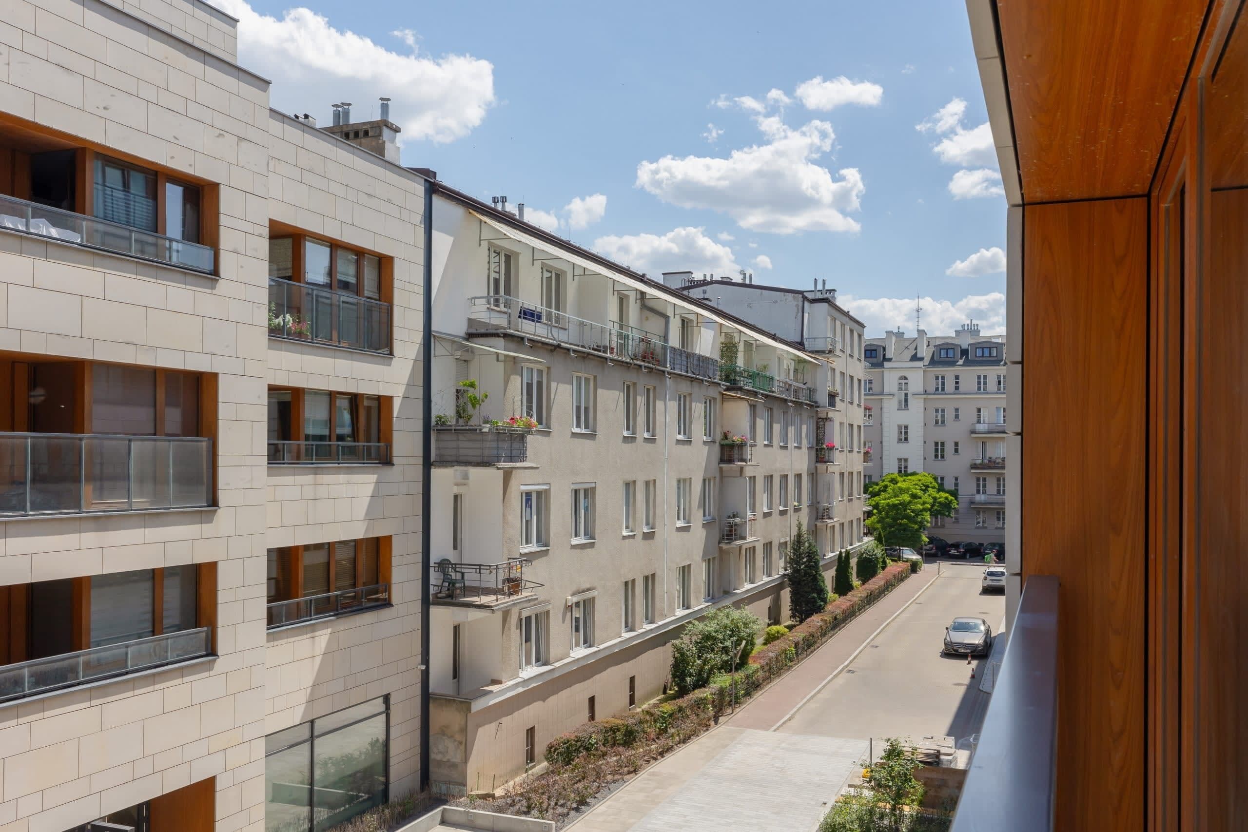 Un immeuble d’appartements moderne doté de nombreux balcons, offrant une vue dégagée sur la rue et comprenant un jardin bien entretenu.