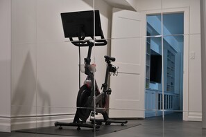 A stationary bike with a screen, located in a room with white walls and a door leading to a staircase.
