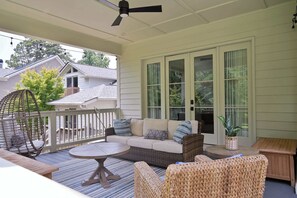 Eine überdachte Veranda mit einer Rattan-Couch, einem runden Tisch und einem Hängesessel.