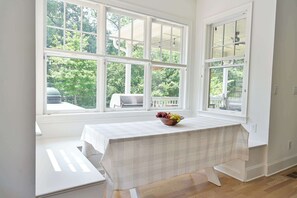 A bright room with large windows, a table with a plaid tablecloth, and a bowl of fruit.