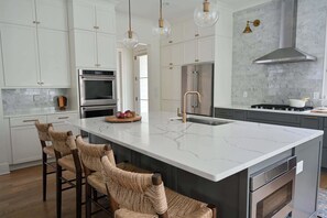 A modern kitchen with white cabinets, a large island, stainless steel appliances, and wicker bar stools.